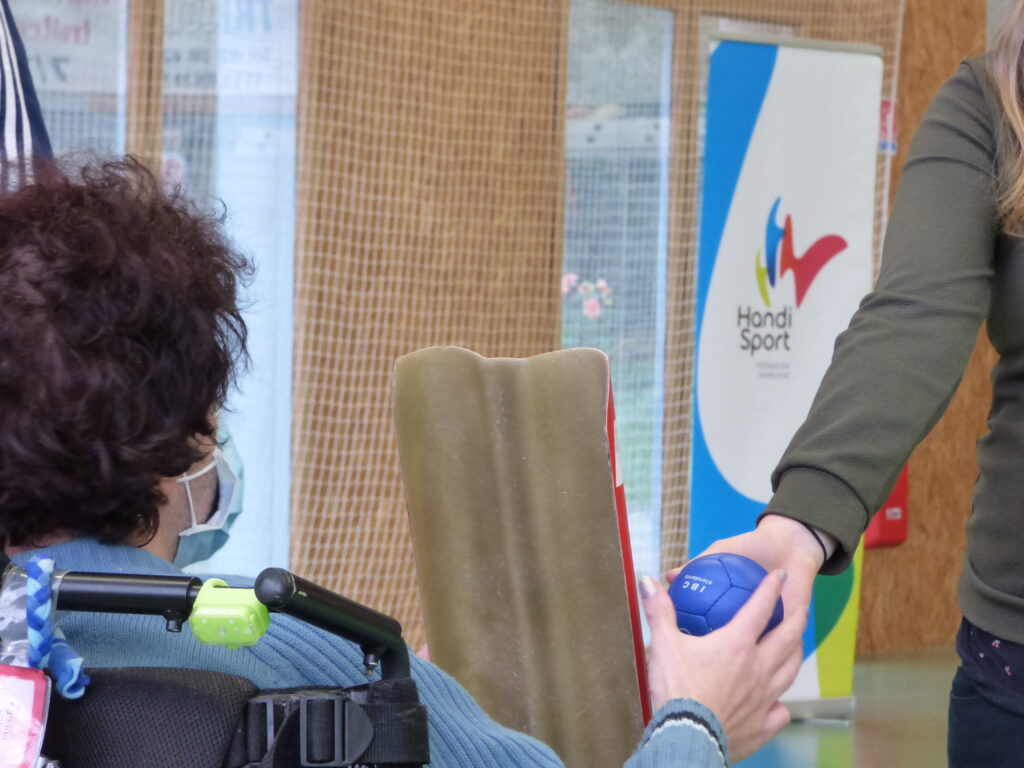 Une éducatrice spécialisée tend une boule de Boccia a un joueur en fauteuil roulant